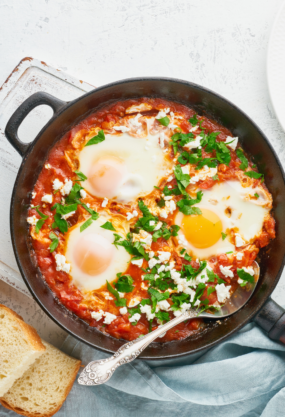 Shakshuka avec œufs pochés, sauce tomate épicée, herbes fraîches et pain grillé, plat traditionnel du Moyen-Orient.