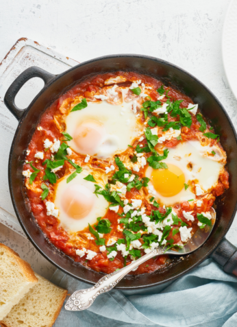 Shakshuka avec œufs pochés, sauce tomate épicée, herbes fraîches et pain grillé, plat traditionnel du Moyen-Orient.