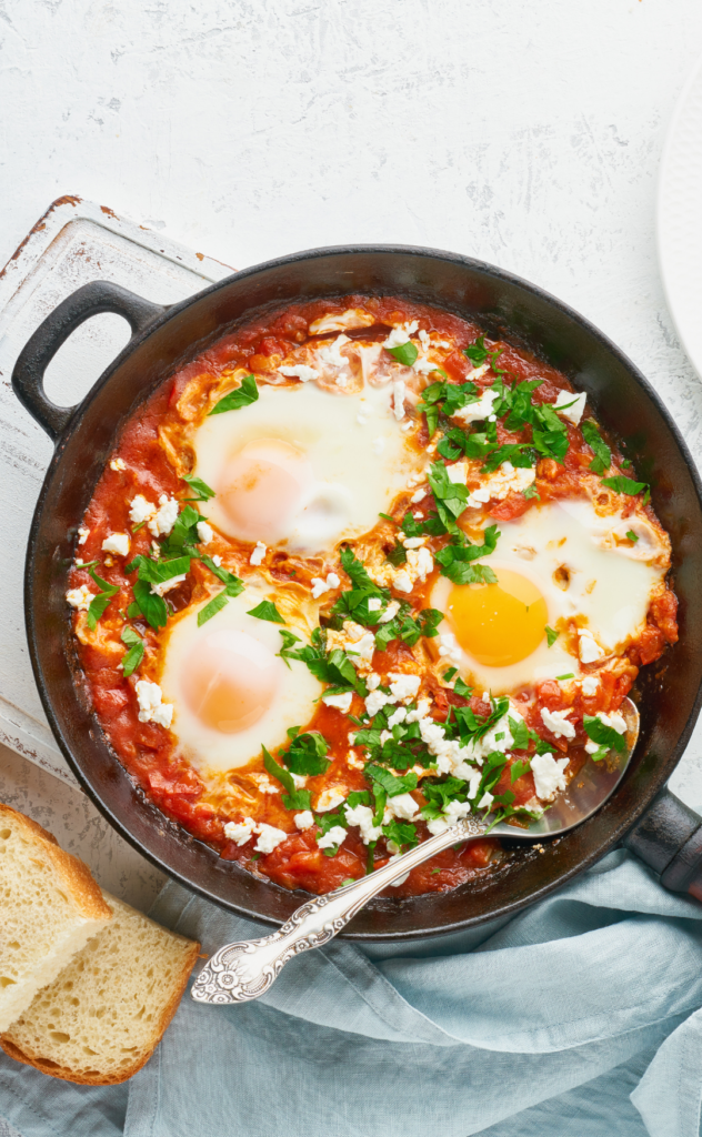 Shakshuka avec œufs pochés, sauce tomate épicée, herbes fraîches et pain grillé, plat traditionnel du Moyen-Orient.