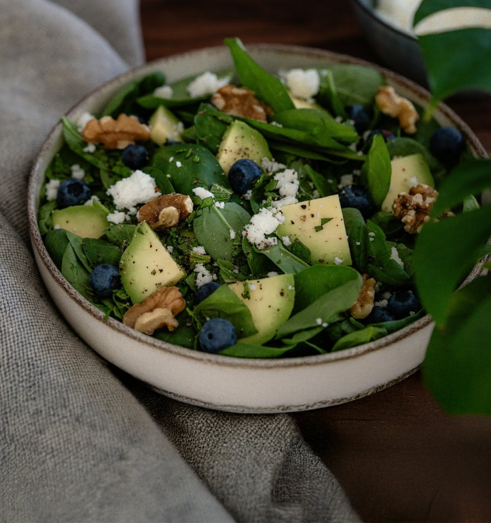 Feuille de salade verte, avocat, myrtilles, noix, fromage frais dans une assiette pour une salade saine et équilibrée, idéale pour une alimentation nutritive.
