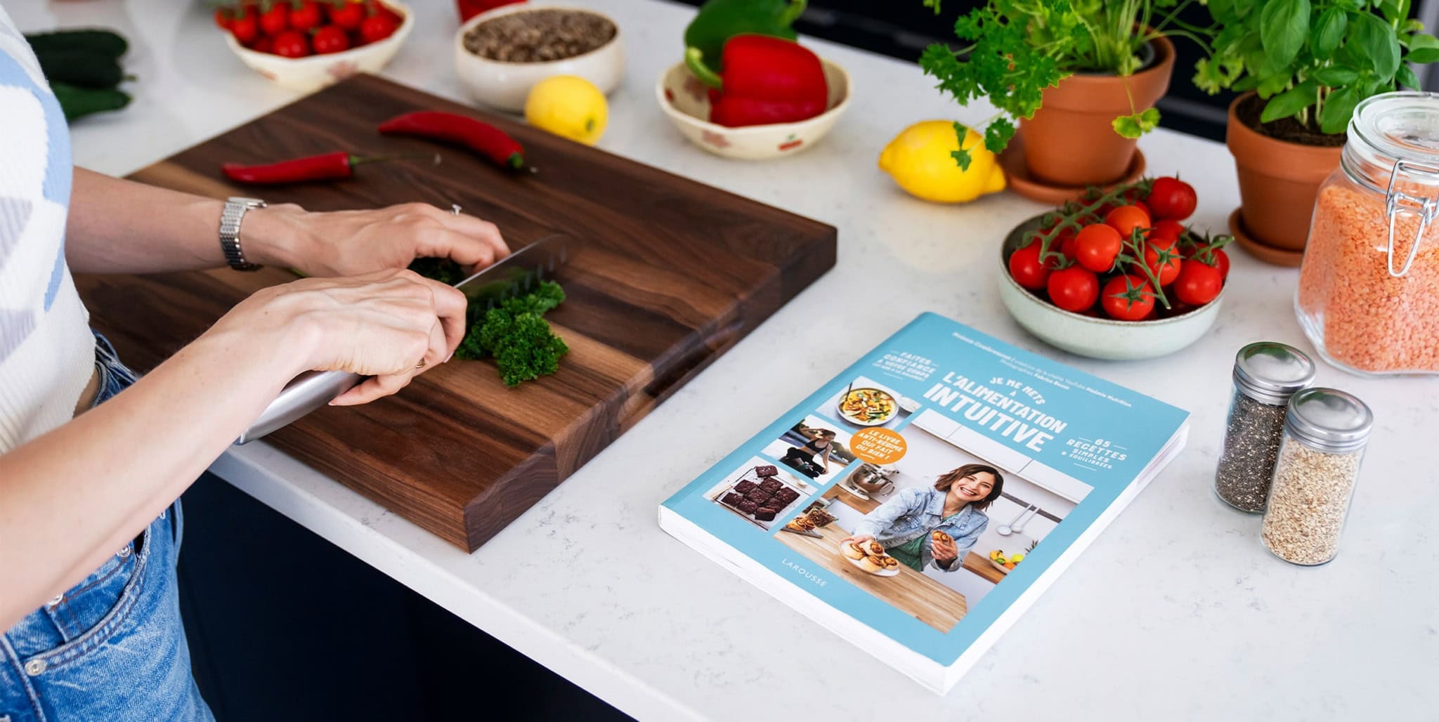 Herbes fraîches coupées sur un plan de travail en bois, dans une cuisine lumineuse avec divers légumes et livres de nutrition, promotion de l'alimentation saine et de la nutrition intuitive.