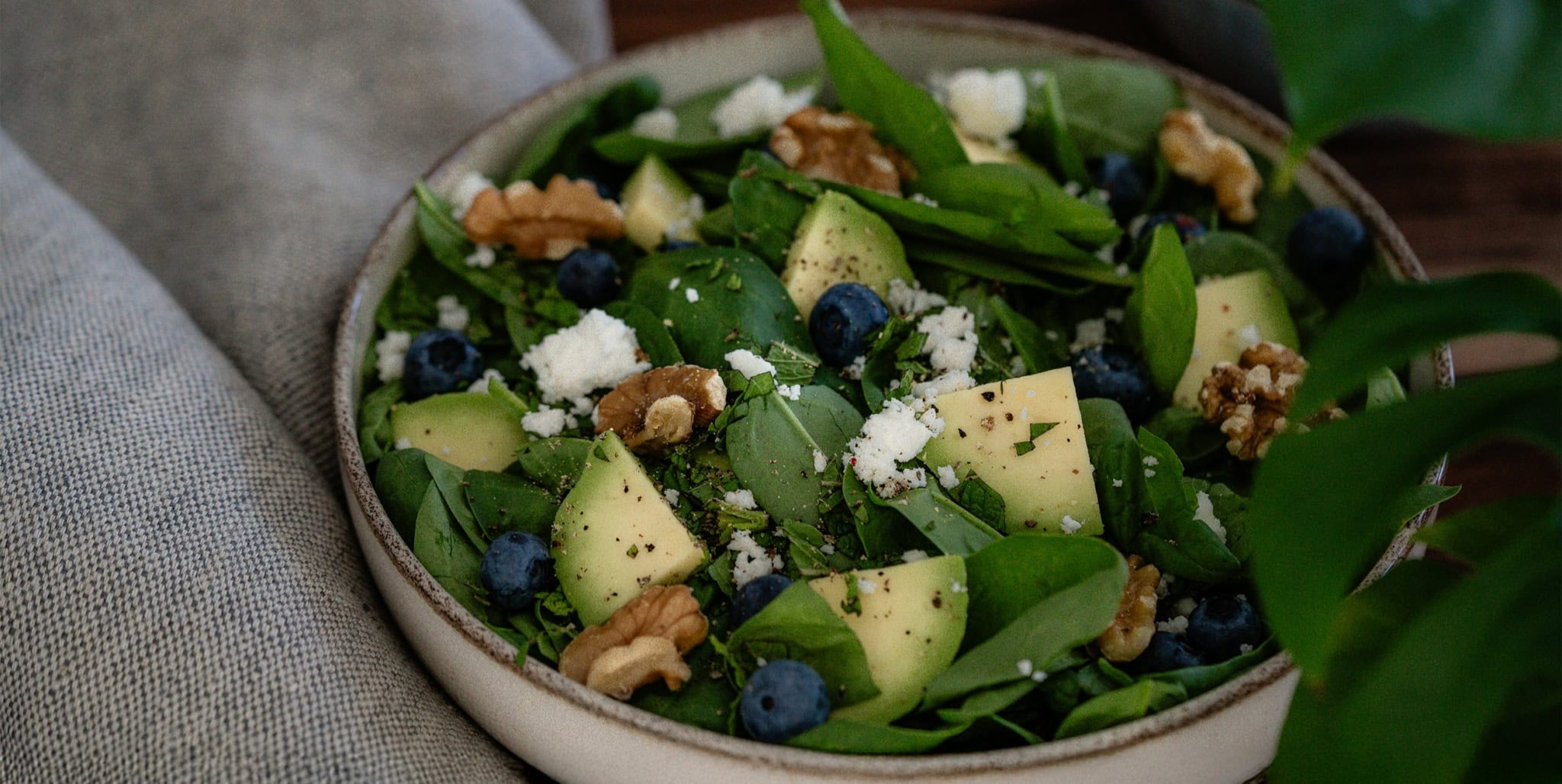 Fresh spinach and avocado salad with blueberries and walnuts, garnished with cheese and herbs, served in a rustic bowl for a nutritious and flavorful meal.