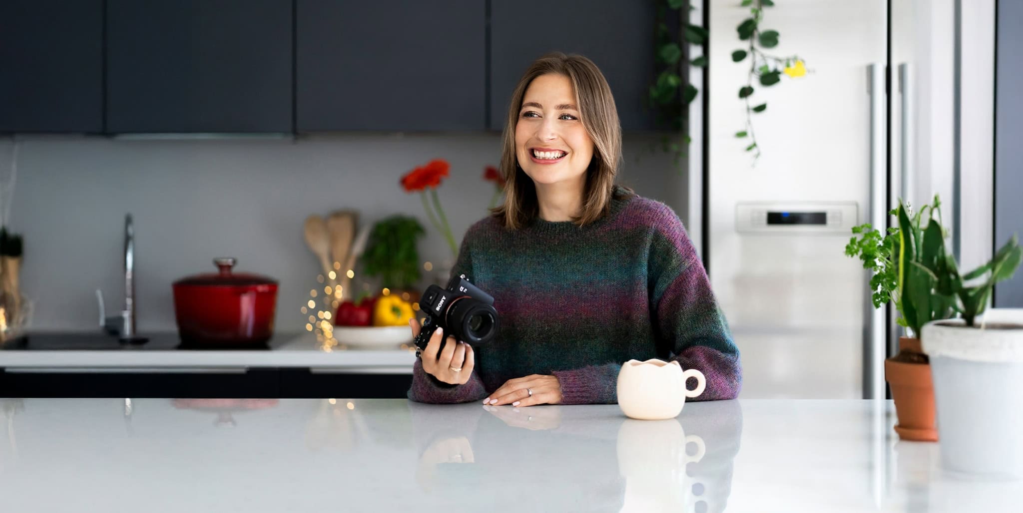 Photographe femme en cuisine, sourire, ambiance chaleureuse, nutrition, cuisine saine, style de vie, design intérieur moderne, bien-être, partage de conseils nutritionnels, photo lifestyle, environnement naturel.