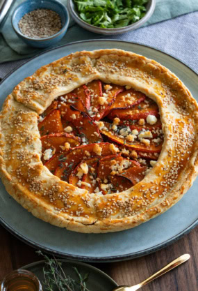 Galette rustique aux légumes, pâte feuilletée, poivrons et fromage, décorée de sesame et herbes fraîches, accompagnée de salade verte, dans une cuisine conviviale, cuisine saine et gourmande.