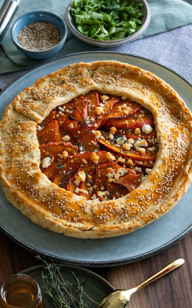 Galette rustique aux légumes, pâte feuilletée, poivrons et fromage, décorée de sesame et herbes fraîches, accompagnée de salade verte, dans une cuisine conviviale, cuisine saine et gourmande.