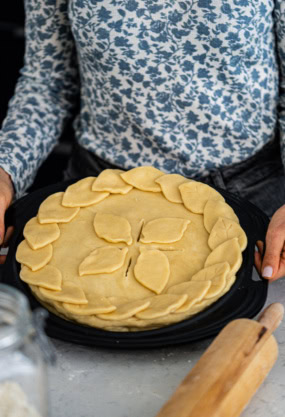Galette de pâte feuilletée avec des décorations de feuilles, prêt à être cuit, sur un plateau noir.