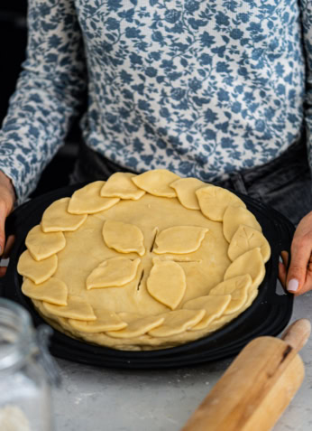 Galette de pâte feuilletée avec des décorations de feuilles, prêt à être cuit, sur un plateau noir.