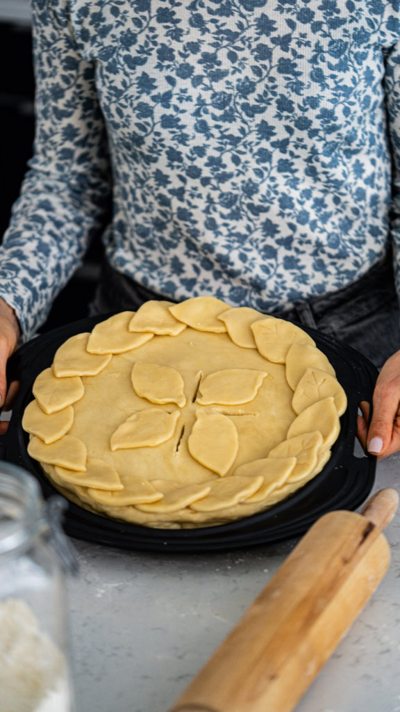 Galette de pâte feuilletée avec des décorations de feuilles, prêt à être cuit, sur un plateau noir.