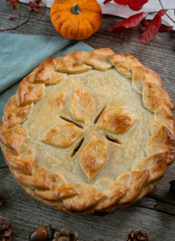 Galette des Rois à la Frangipane, pâtisserie traditionnelle de l'automne, décorée de feuilles en pâte feuilletée, entourée de décorations automnales comme des petits pumpkins, des pommes de pin et des châtaignes.
