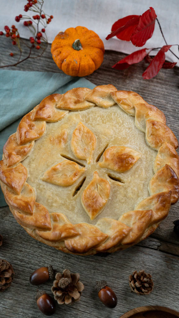 Galette des Rois à la Frangipane, pâtisserie traditionnelle de l'automne, décorée de feuilles en pâte feuilletée, entourée de décorations automnales comme des petits pumpkins, des pommes de pin et des châtaignes.