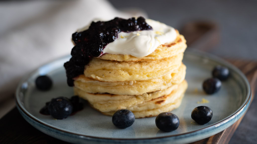 Pancakes moelleux, garnis de crème fraîche et mûres fraîches, servis sur une assiette élégante, parfaits pour un petit-déjeuner sain ou une pause gourmande.
