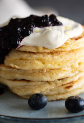 Pancakes moelleux, garnis de crème fraîche et mûres fraîches, servis sur une assiette élégante, parfaits pour un petit-déjeuner sain ou une pause gourmande.