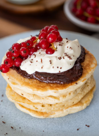 Pancakes faits maison avec chocolat, crème fouettée, et groseilles rouges fraîches, petit déjeuner gourmand sain, recette bio pour nutrition équilibrée, petit déjeuner healthy, aliment riche en vitamines, snack nutritif naturel.