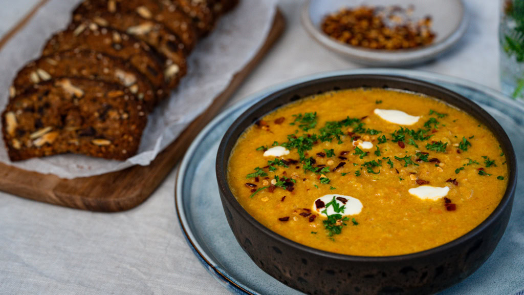 Soupe de lentilles corail épicée avec crème et coriandre garnie, accompagnée de pain aux noix sur une planche en bois, prêt à déguster, idéal pour une alimentation saine et équilibrée, recettes végétariennes nutritives.