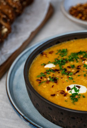 Soupe de lentilles corail épicée avec crème et coriandre garnie, accompagnée de pain aux noix sur une planche en bois, prêt à déguster, idéal pour une alimentation saine et équilibrée, recettes végétariennes nutritives.