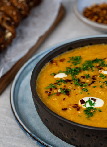 Soupe de lentilles corail épicée avec crème et coriandre garnie, accompagnée de pain aux noix sur une planche en bois, prêt à déguster, idéal pour une alimentation saine et équilibrée, recettes végétariennes nutritives.