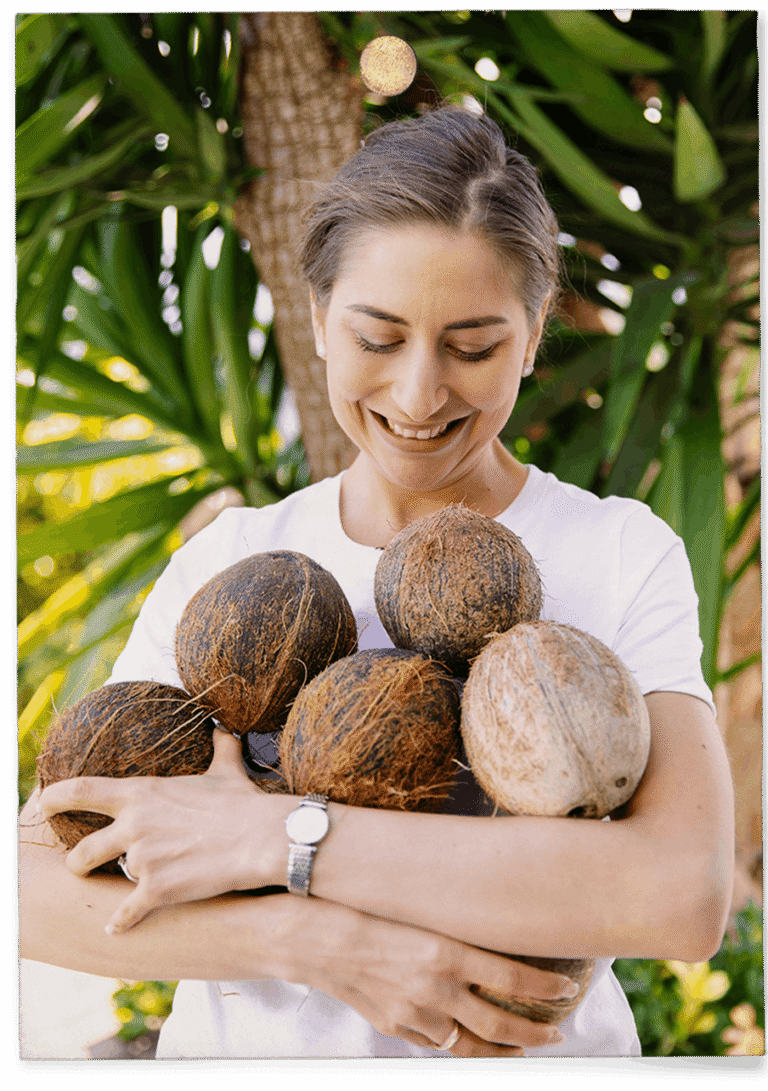 Coconuts tropicaux dans les bras d'une femme en extérieur, symbolisant la nutrition saine et naturelle.