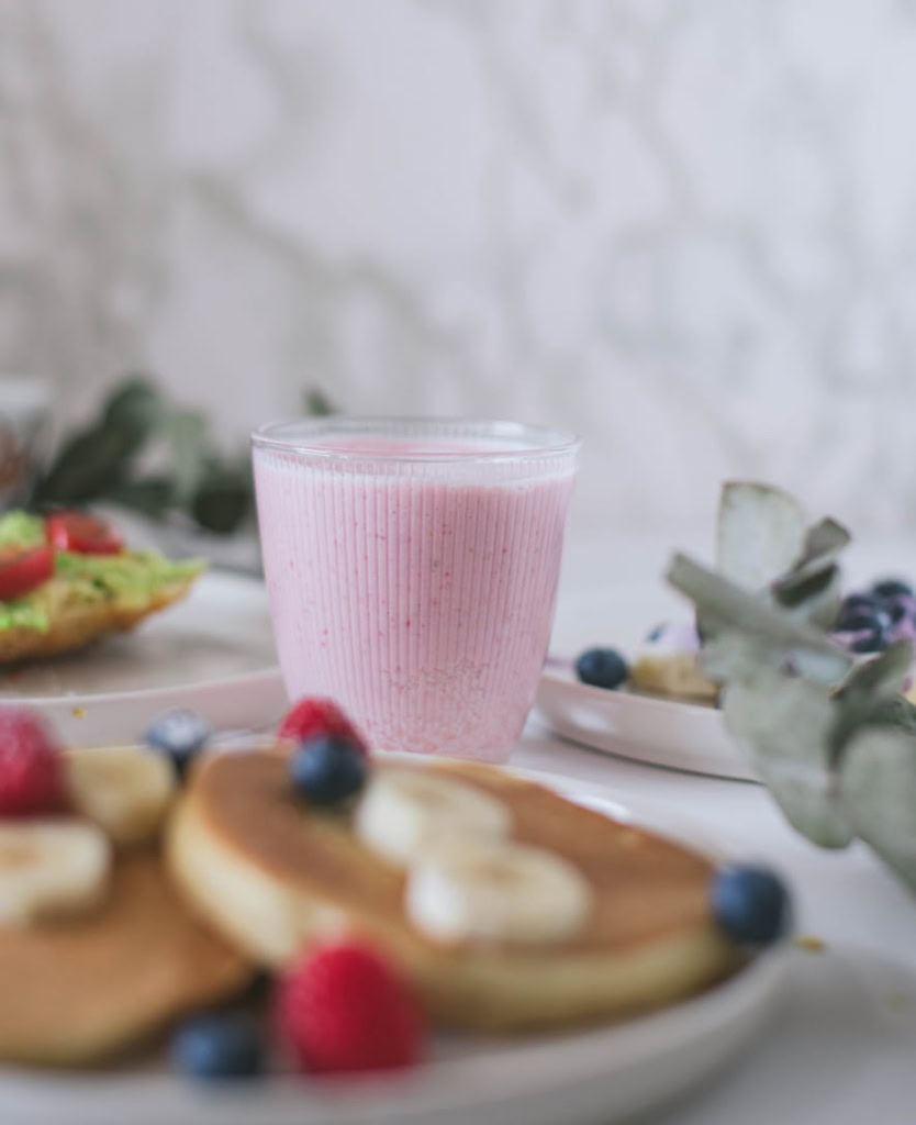 Pancakes aux fruits frais avec bananes, myrtilles et framboises, accompagnés d'un smoothie aux fruits rouges dans un verre transparent.